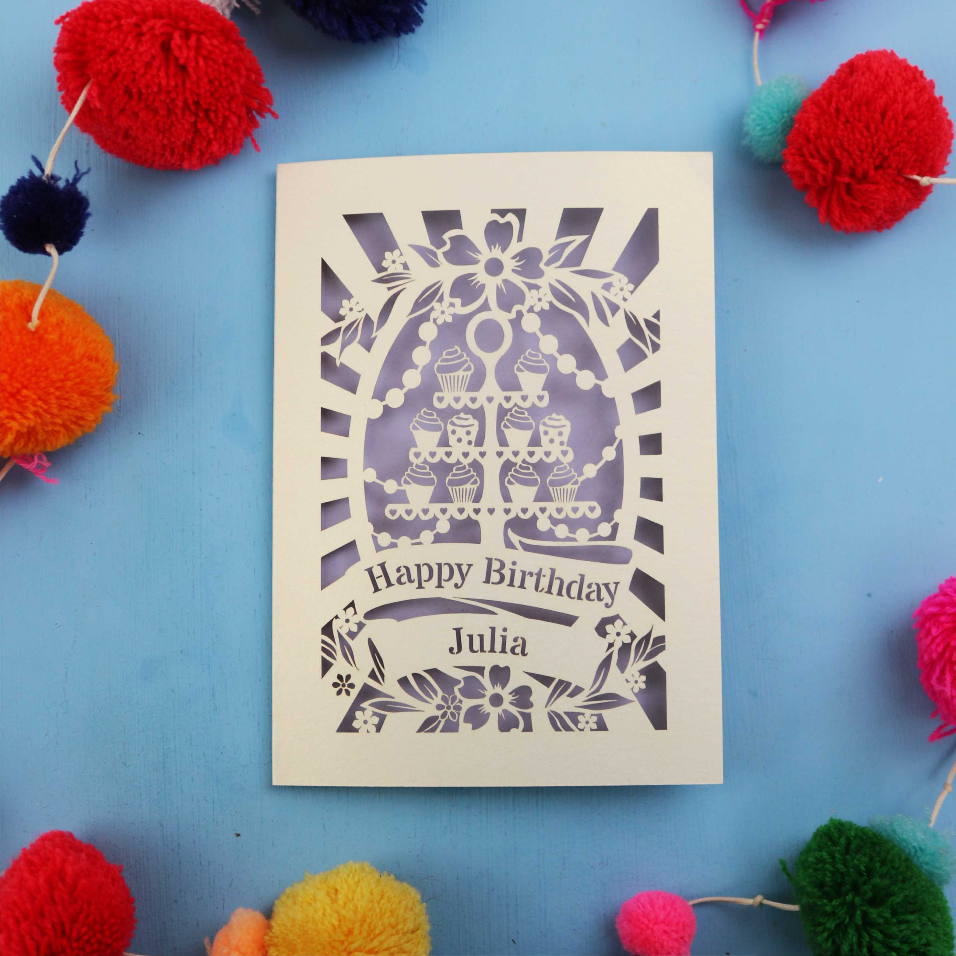 Personalized birthday card with decorative elements on a blue background with colourful pom-poms.