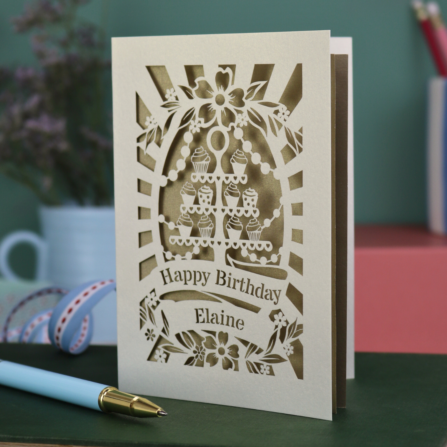 Laser-cut birthday card with cake design and 'Happy Birthday Elaine' text on a green surface.