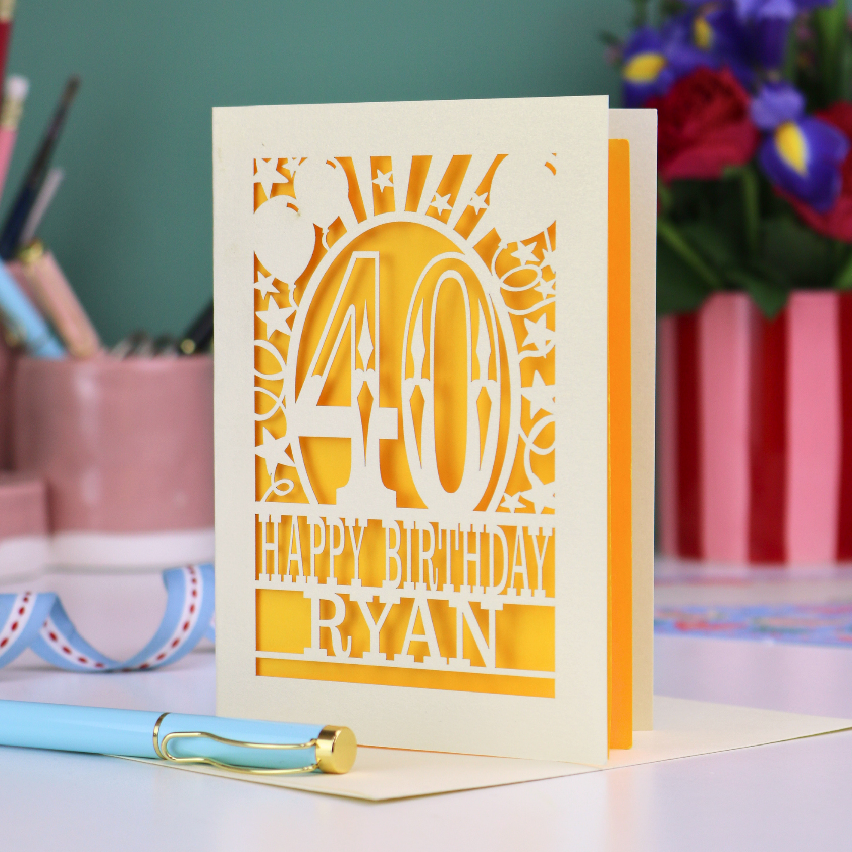 Personalized 40 birthday card with '40 Happy Birthday Ryan' on a desk with stationery items.