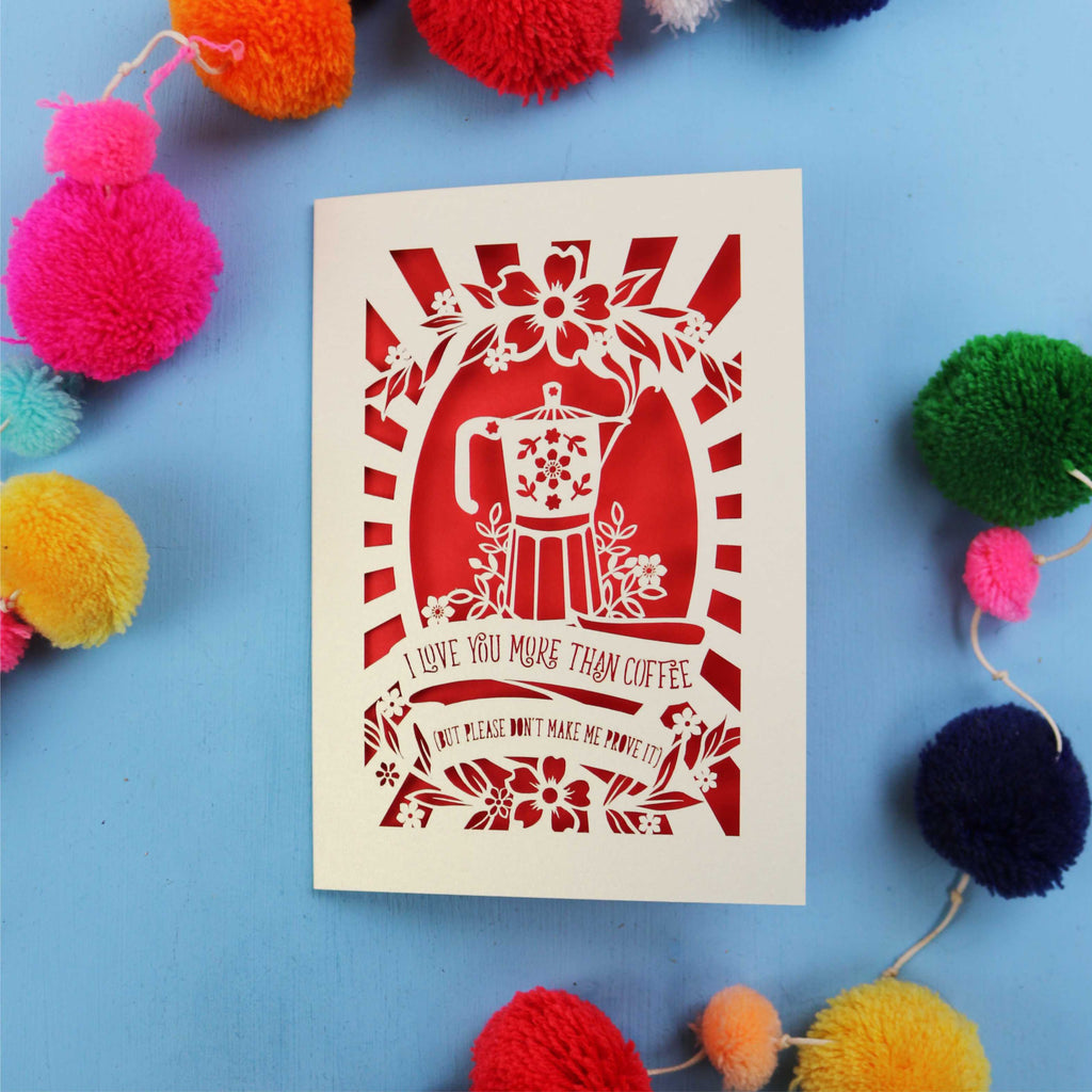 Decorative funny Valentine's card with coffee-themed design and the words "I love you more than coffee, but please don't make me prove it)" on a blue background with colourful pom-poms.