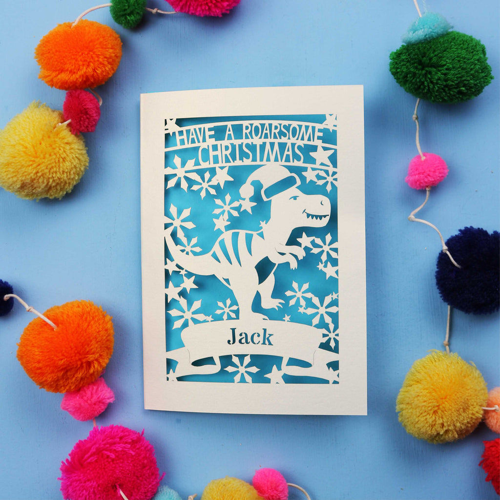 Christmas card with dinosaur design and colourful pom-poms on a blue background