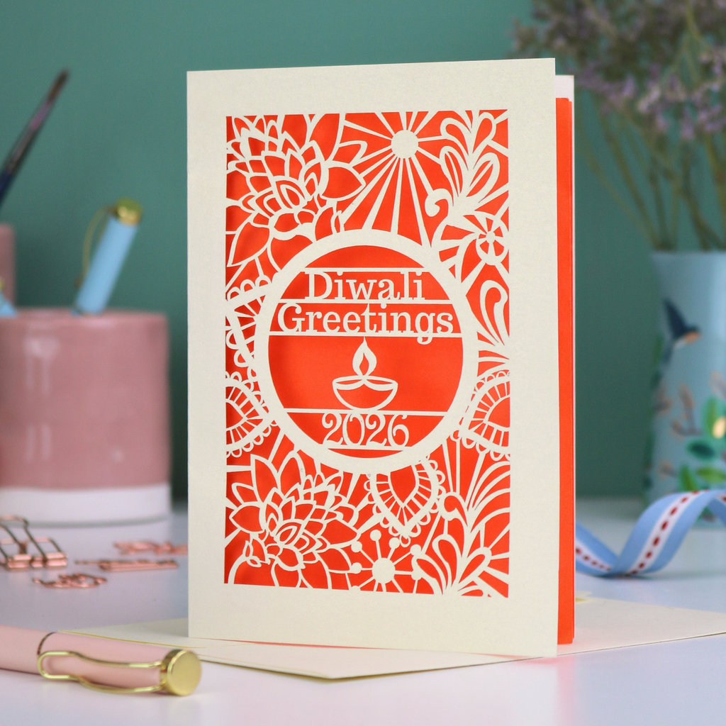 Paper Cut Diwali greetings card with intricate design and 'Diwali Greetings 2026' text on a desk.