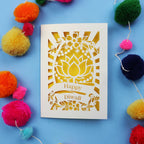 Decorative laser cut Diwali card with 'Happy Diwali' text on a blue background with colourful pom-poms.