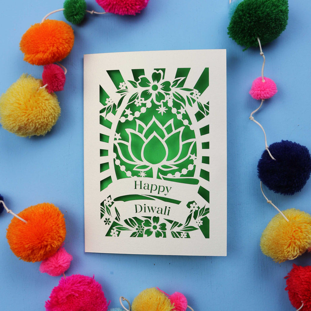 Decorative laser cut Diwali card with 'Happy Diwali' text on a blue background with colourful pom-poms.