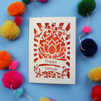 Decorative laser cut Diwali card with 'Happy Diwali' text on a blue background with colourful pom-poms.