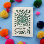 Decorative laser cut Diwali card with 'Happy Diwali' text on a blue background with colourful pom-poms.