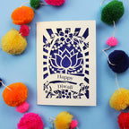 Decorative laser cut Diwali card with 'Happy Diwali' text on a blue background with colourful pom-poms.