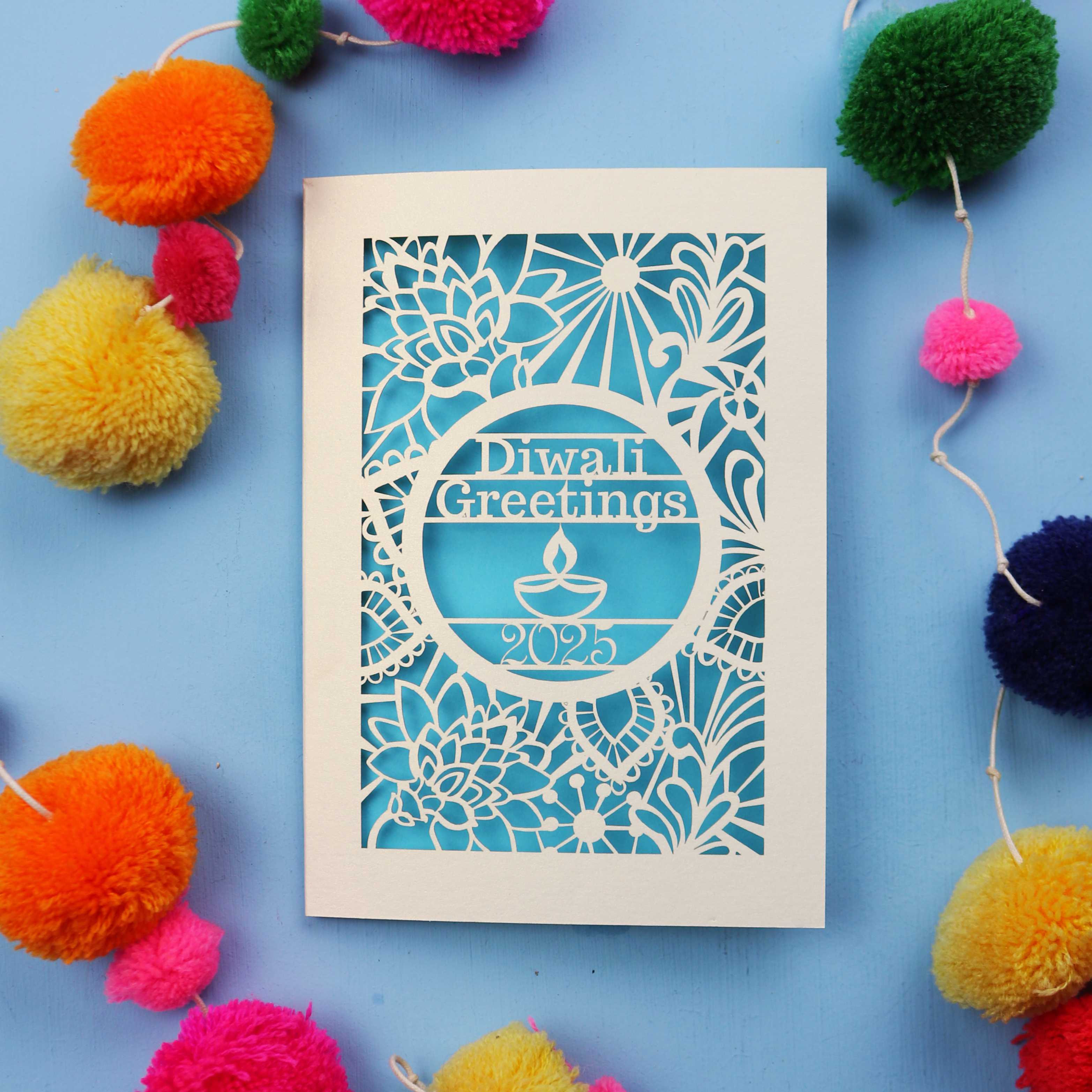 Decorative card with 'Diwali Greetings 2025' text on a blue background with colourful pom-poms.