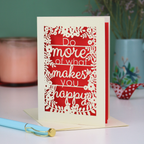 Motivational card with text 'Do more of what makes you happy' on a red background, placed on a surface with a pen and decorative items.