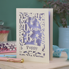 Congratulations card laser cut with 'Dream Big Poppy' text on a wooden surface with decorative items.