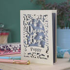 Decorative cut out card with 'Dream Big Poppy' text on a wooden surface with a blurred background
