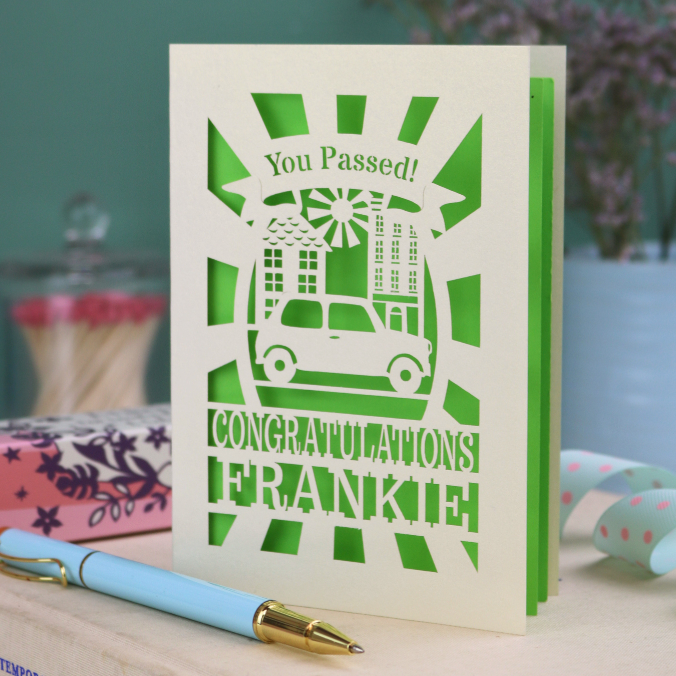 Laser-cut Driving Test Congratulations card with 'You Passed! Congratulations Frankie' text on a wooden surface with a pen.
