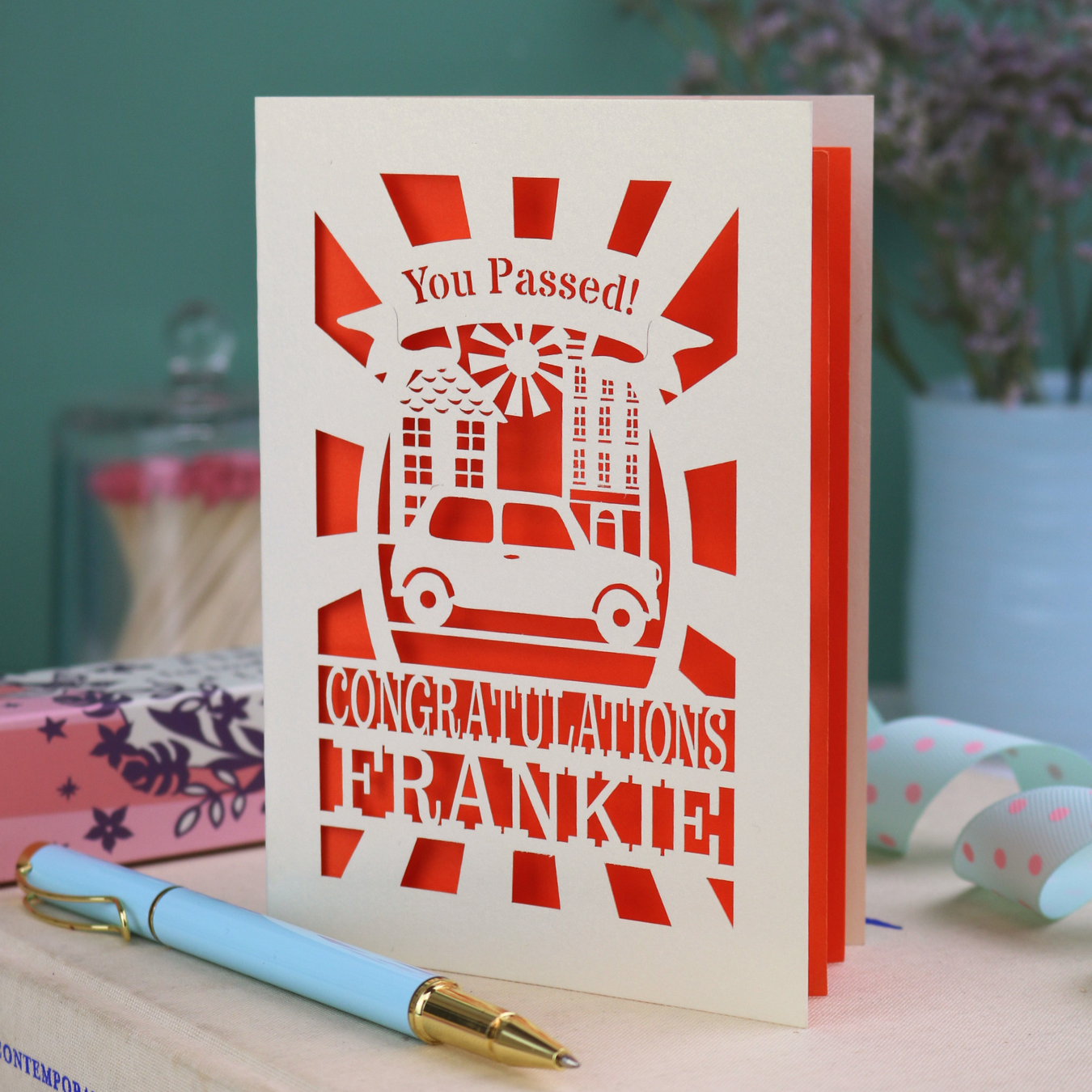 Laser-cut Driving Test card with 'You Passed! Congratulations Frankie' text on a wooden surface with a pen.