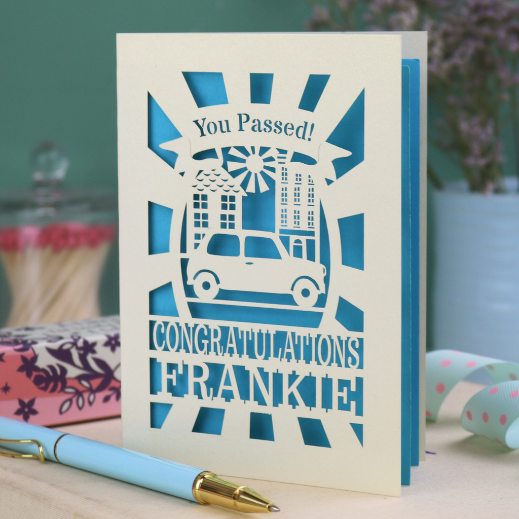 Laser-cut Driving Test Pass card with 'You Passed! Congratulations Frankie' text on a wooden surface with a pen.