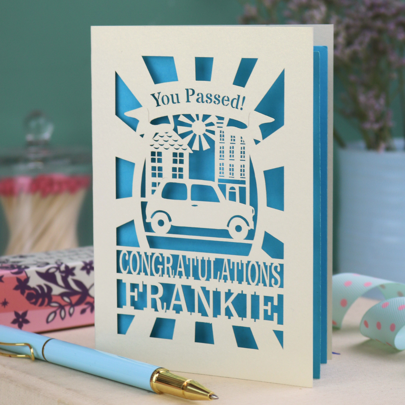 Laser-cut Driving Test Pass card with 'You Passed! Congratulations Frankie' text on a wooden surface with a pen.