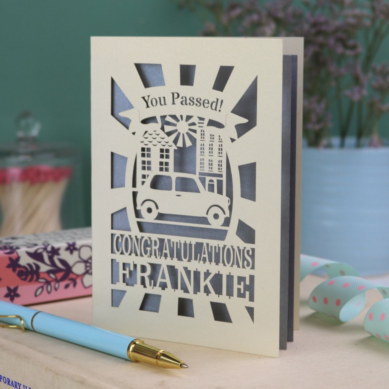 Laser-cut Driving Test Congratulations card with 'You Passed! Congratulations Frankie' text on a wooden surface with a pen.