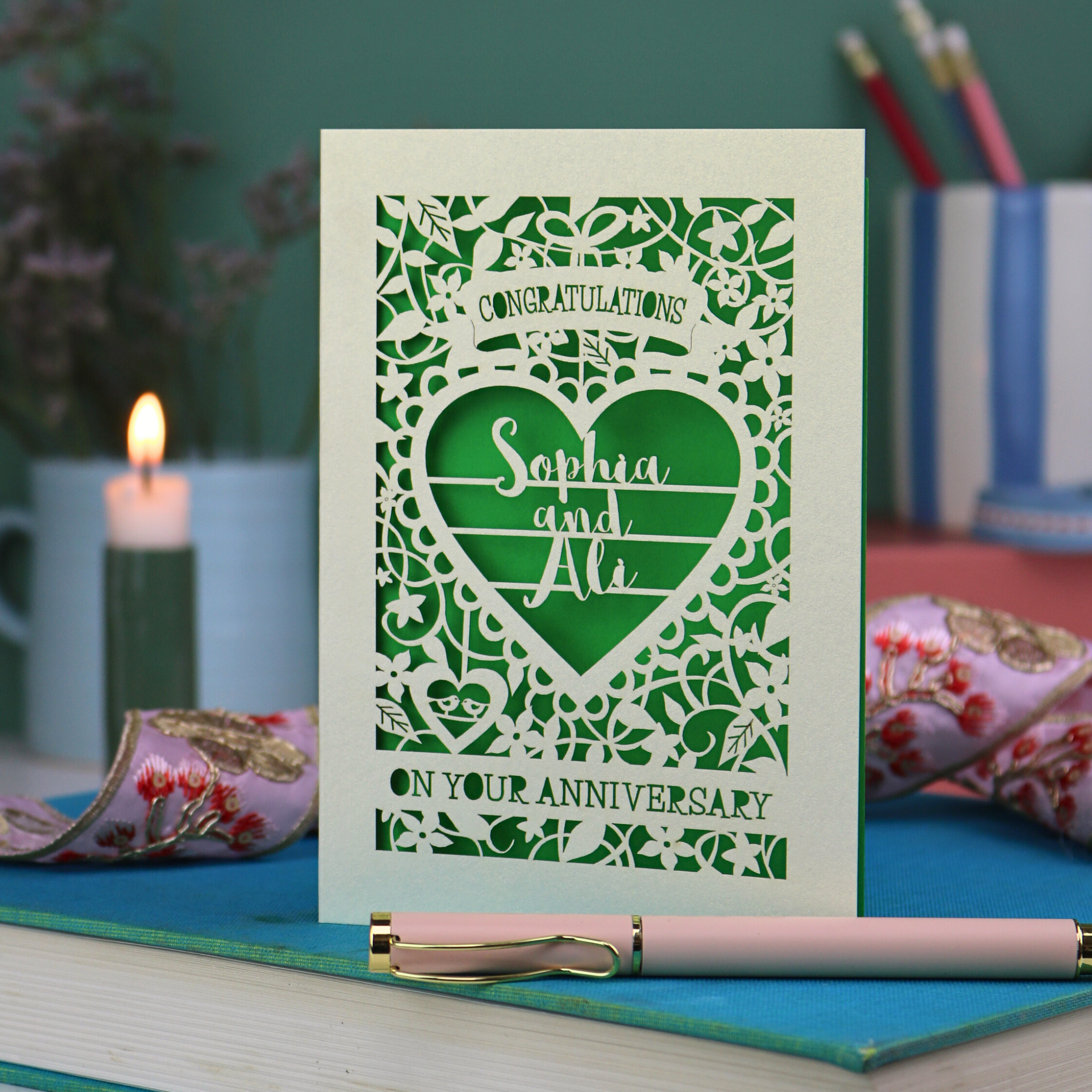 Laser cut Anniversary card with decorative heart design on a table with stationery items.