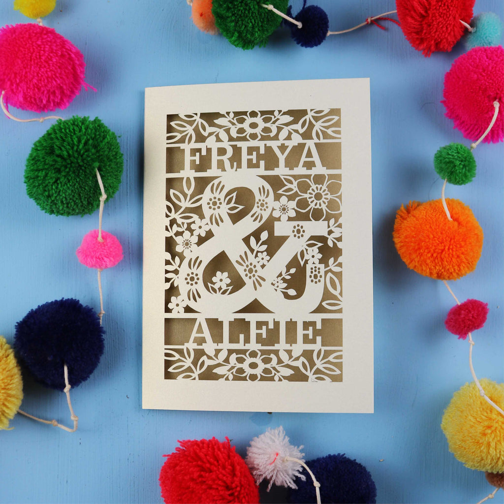 Decorative card with cut-out names surrounded by colourful pom-poms on a blue background