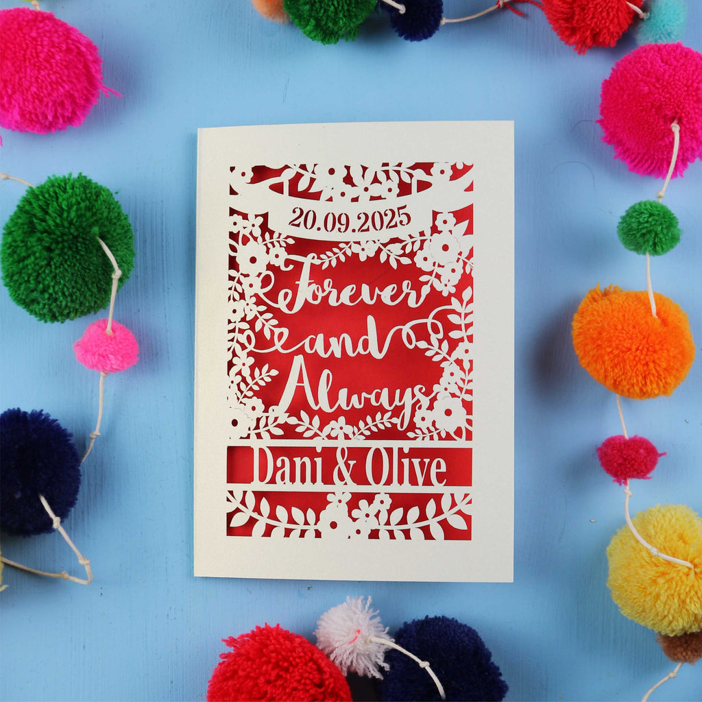 Decorative laser cut engagement card with personalized text on a blue background with colourful pom-poms.