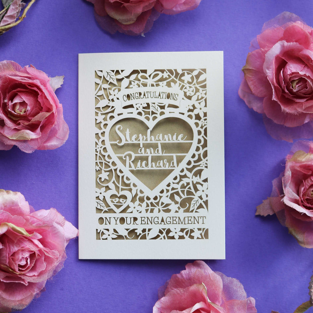 A cream and gold engagement card featuring names and flowers 
