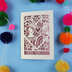 Decorative engagement card with cut-out design and 'The Lovers' text on a blue background with colourful pom-poms.
