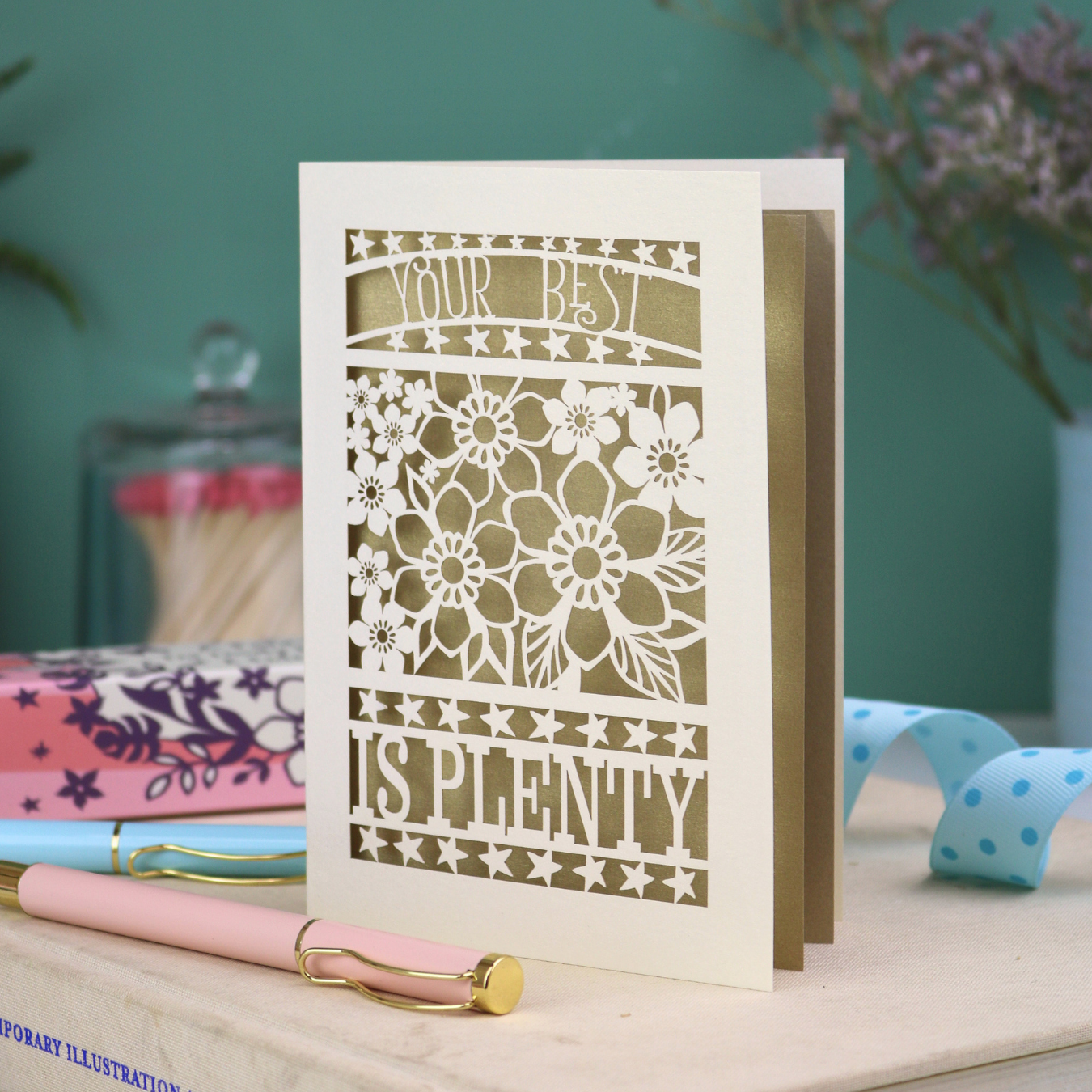 Decorative laser cut greetings card with floral design and text, 'Your best is plenty' on a table with stationery items.