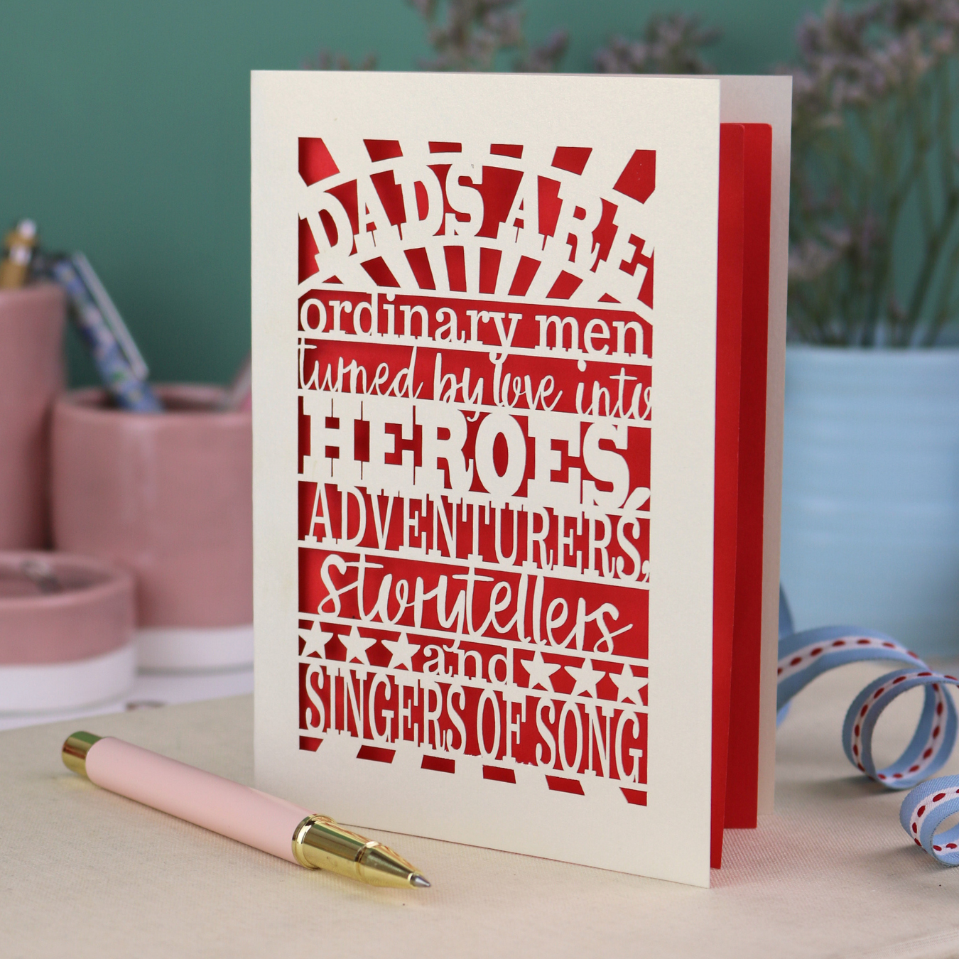 A laser cut father's Day card with cut out quote, "Dads are ordinary men turned by love into heroes, adventurers, storytellers and singers of song", with a cream card and bright red paper insert