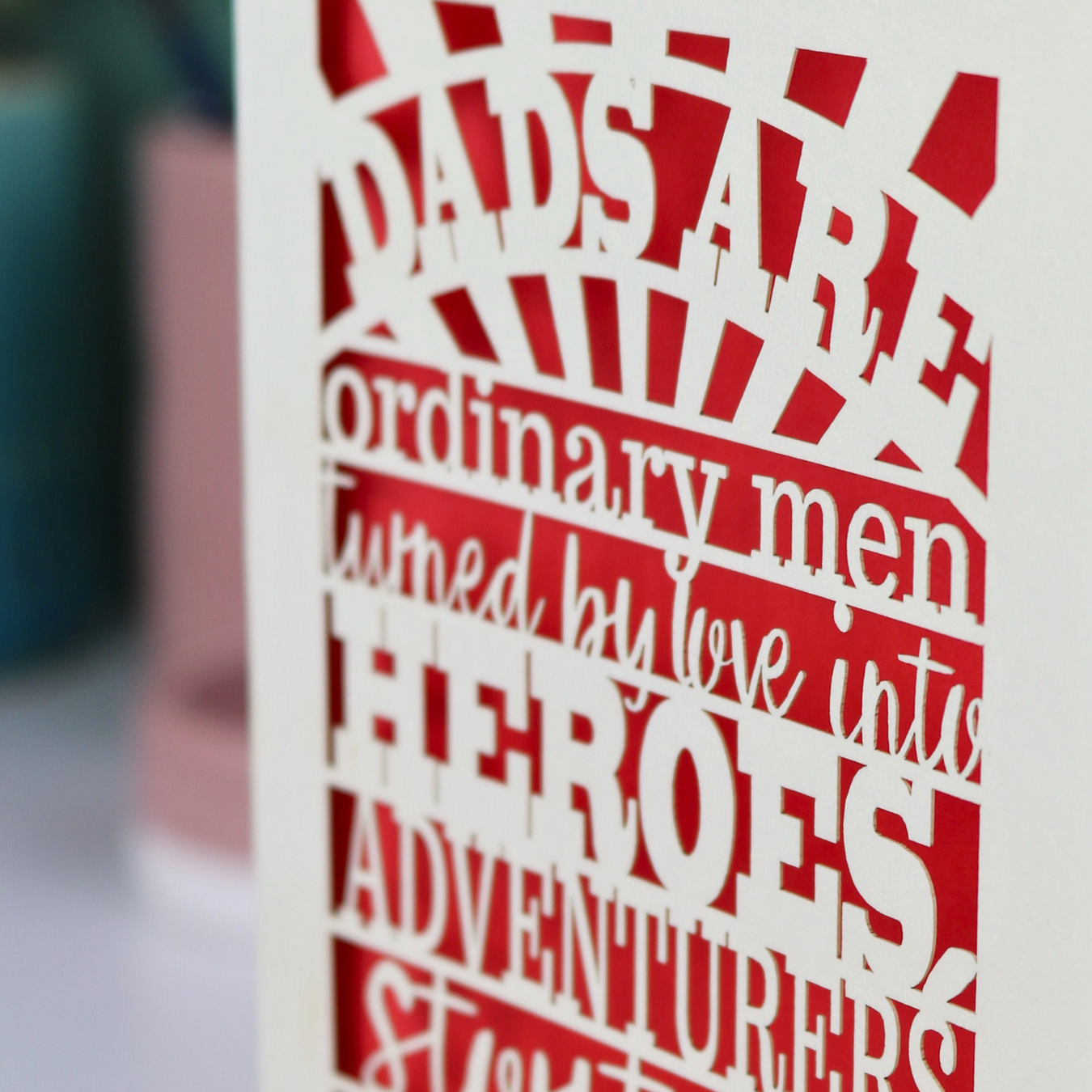 A laser cut father's Day card with cut out quote, "Dads are ordinary men turned by love into heroes, adventurers, storytellers and singers of song", with a cream card and bright red paper insert