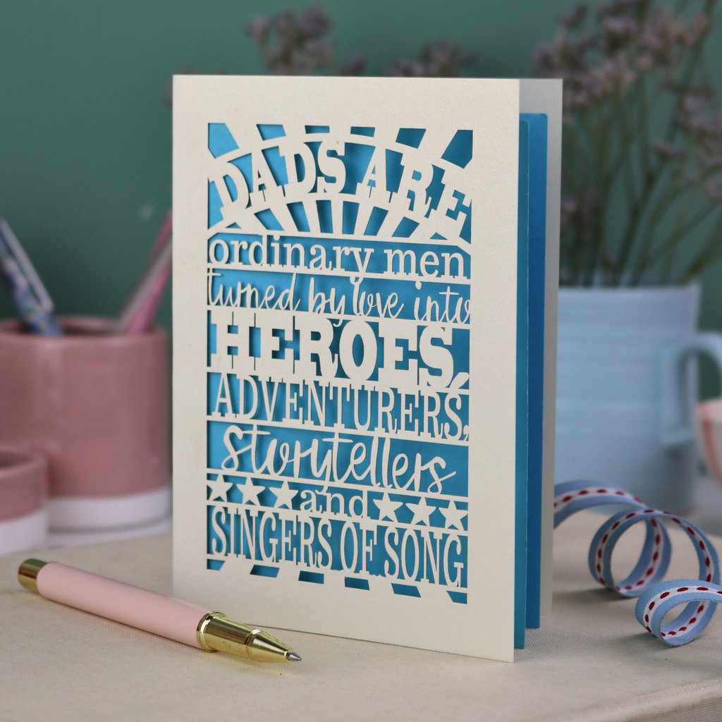 A laser cut father's Day card with cut out quote, "Dads are ordinary men turned by love into heroes, adventurers, storytellers and singers of song", with a cream card and bright blue paper insert