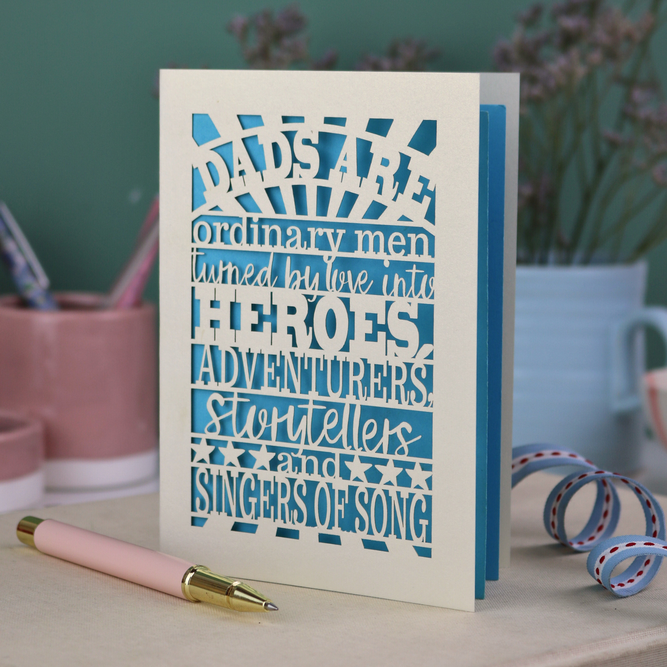 A laser cut father's Day card with cut out quote, "Dads are ordinary men turned by love into heroes, adventurers, storytellers and singers of song", with a cream card and bright blue paper insert