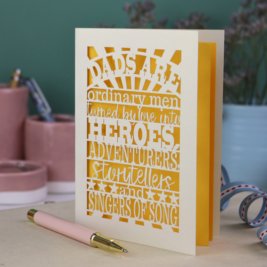 A laser cut father's Day card with cut out quote, "Dads are ordinary men turned by love into heroes, adventurers, storytellers and singers of song", with a cream card and bright yellow paper insert