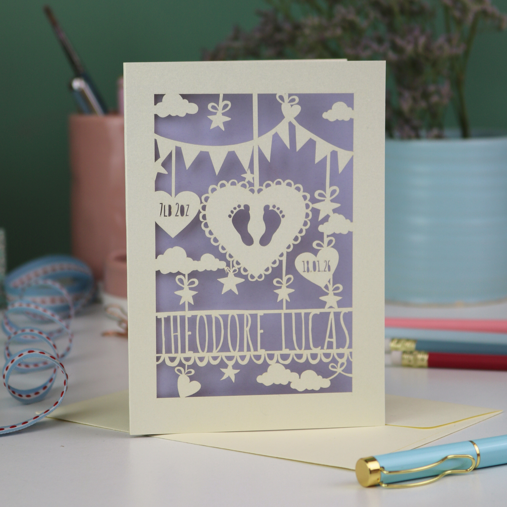Decorative baby card with cut-out designs on a desk with stationery items.