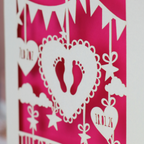 Decorative baby card with cut-out designs on a pink background