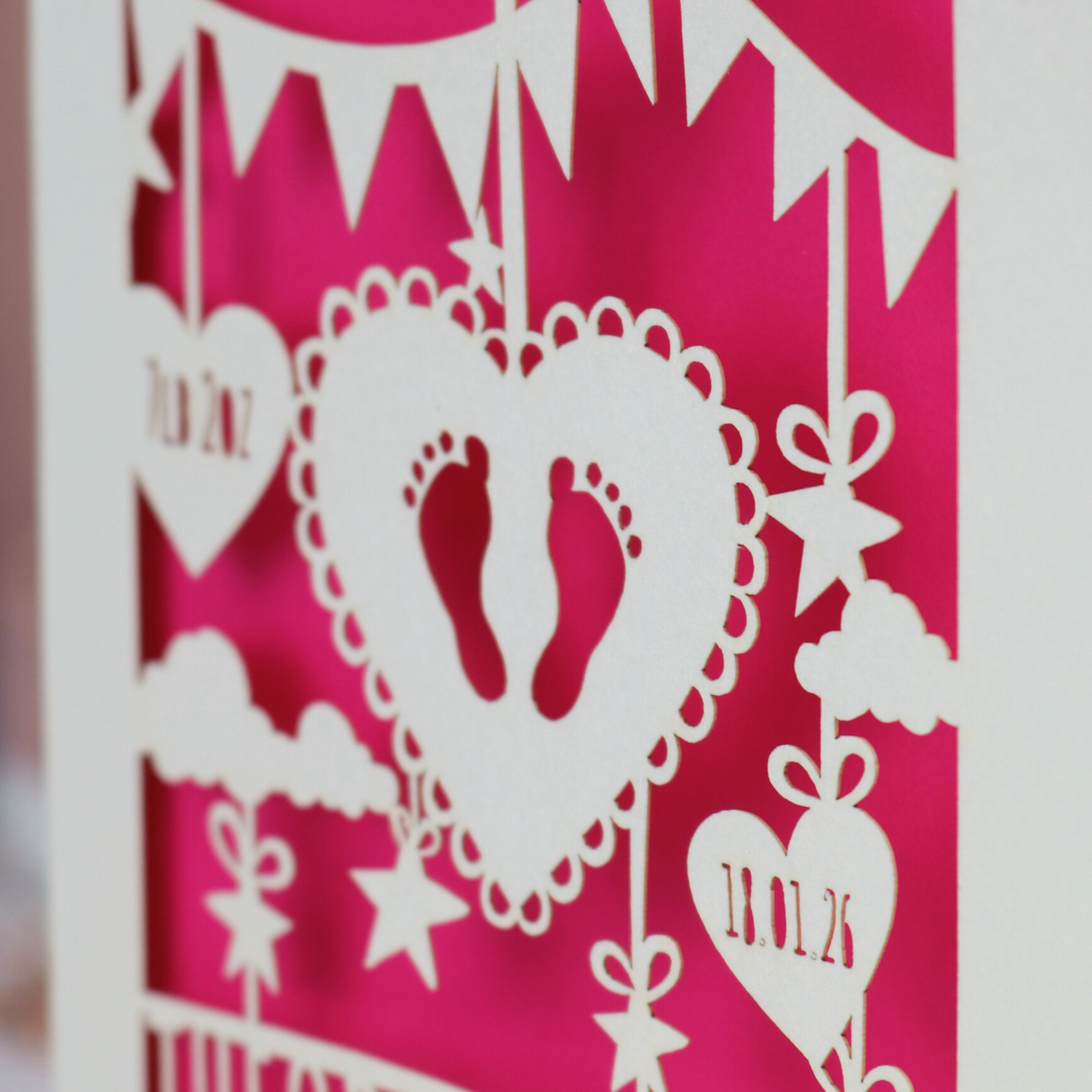 Decorative baby card with cut-out designs on a pink background