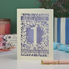 Greetings Card with '1 amazing year' text on a table with candles and a plant in the background