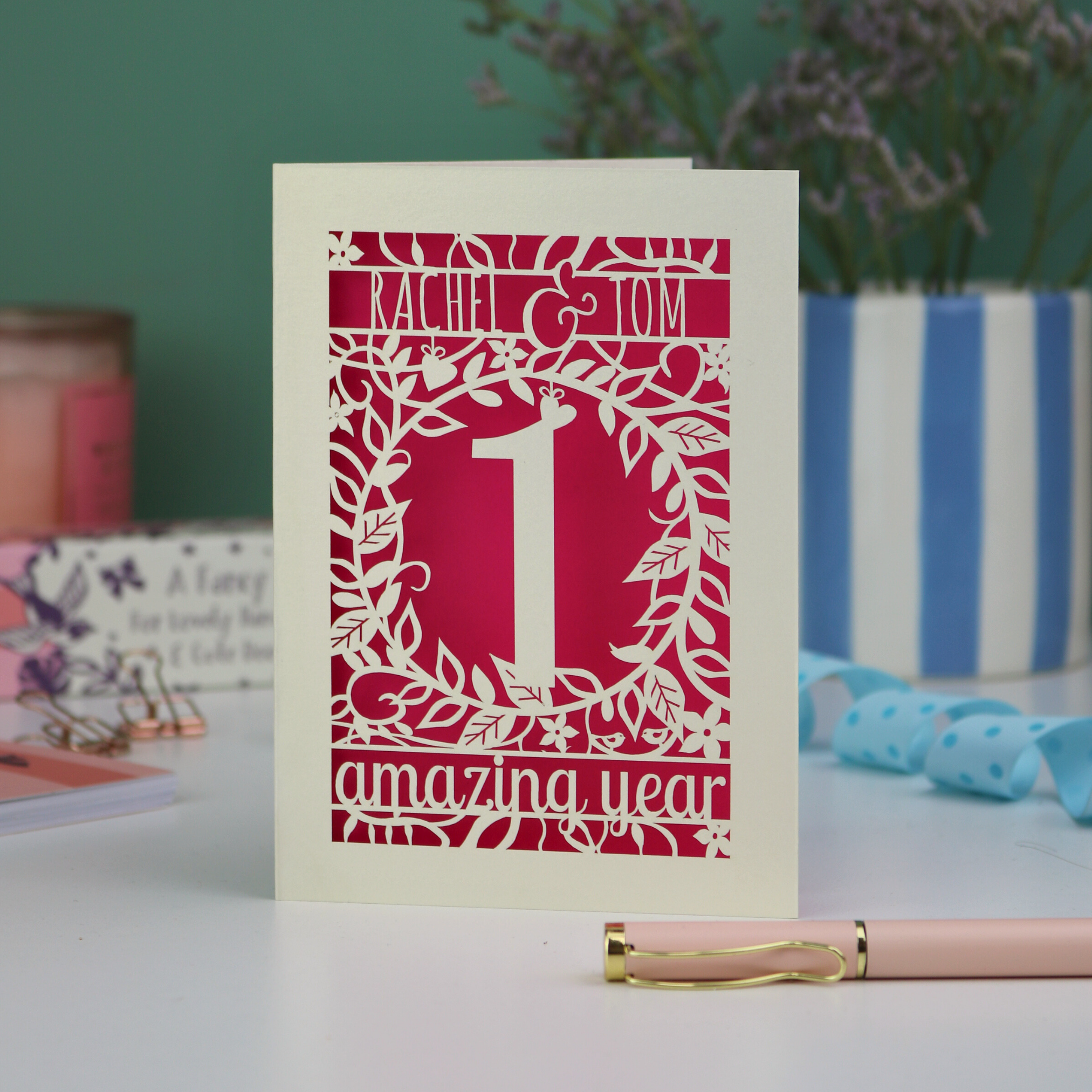 first anniversary Card with '1 amazing year' design on a table with a pen and decorative items.