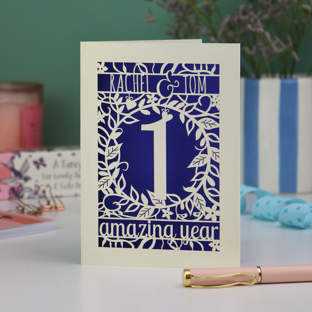 first anniversary Card with '1 amazing year' design on a table with a pen and decorative items.