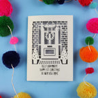 Christmas in your new home Card with festive design on a blue background with colourful pom-poms