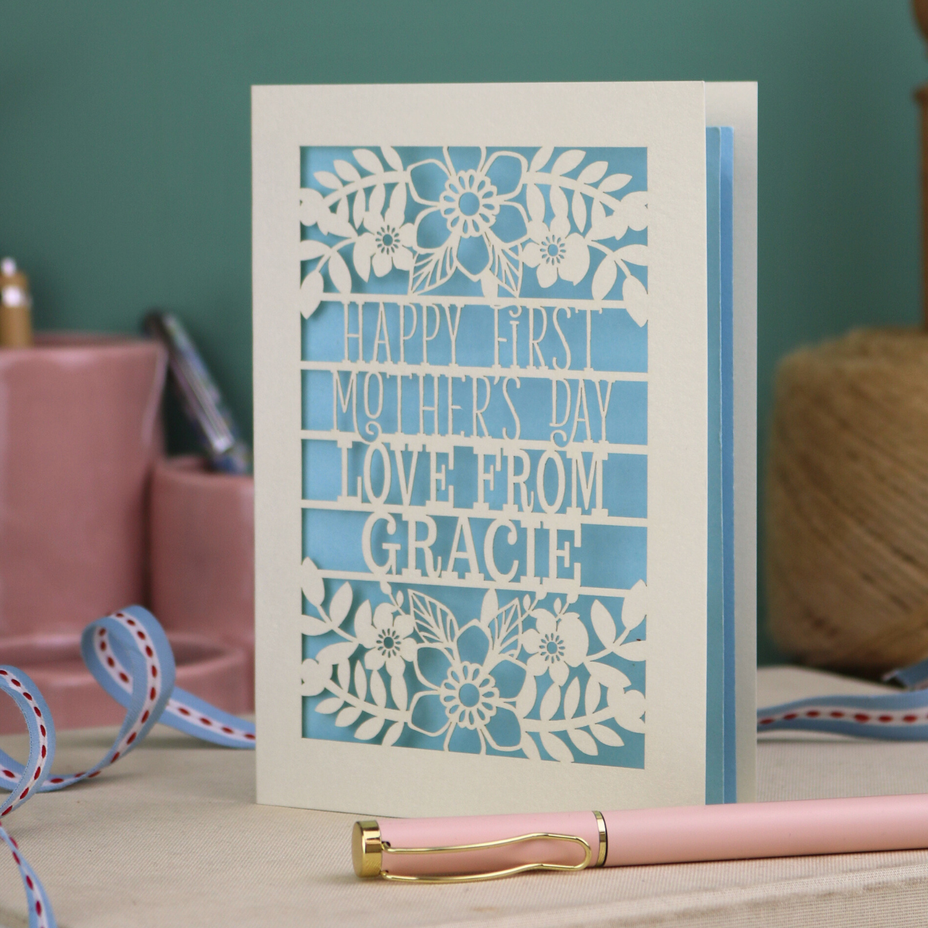 A floral laser cut 1st mother's day card with cut out text, "Happy First Mother's Day Love From" and is personalised with a name. 