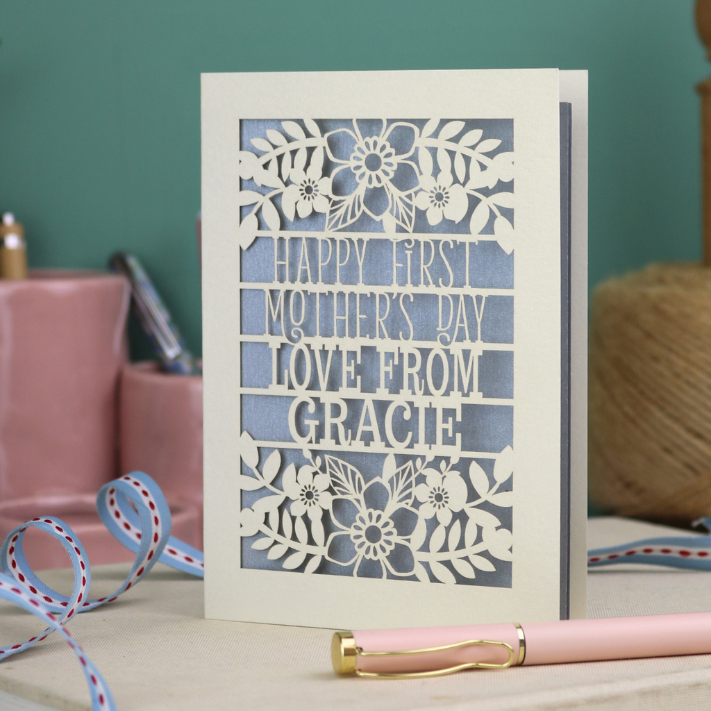 A floral laser cut 1st mother's day card with cut out text, "Happy First Mother's Day Love From" and is personalised with a name. 