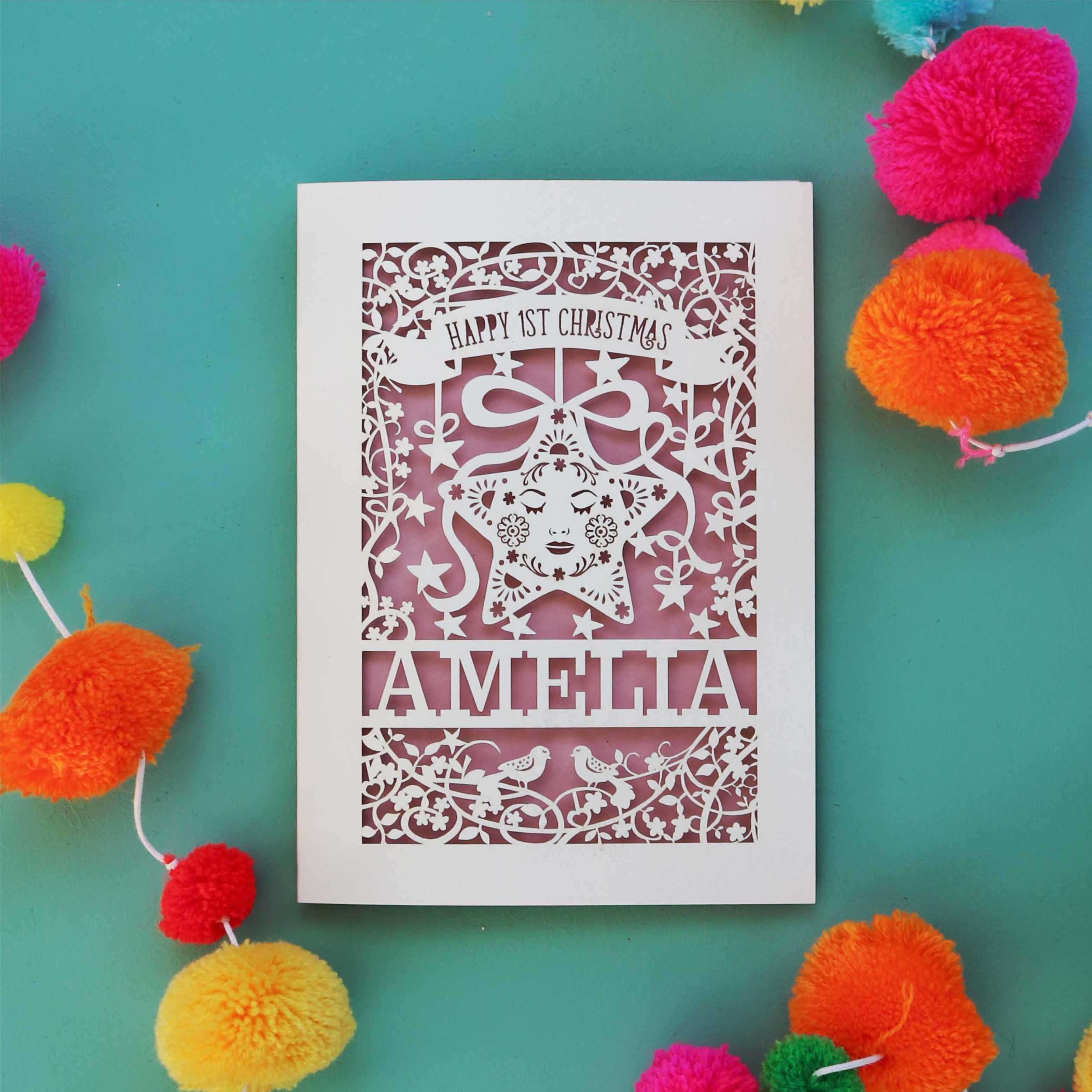 A laser cut first Christmas card personalised with a name and featuring a star surrounded by a floral border