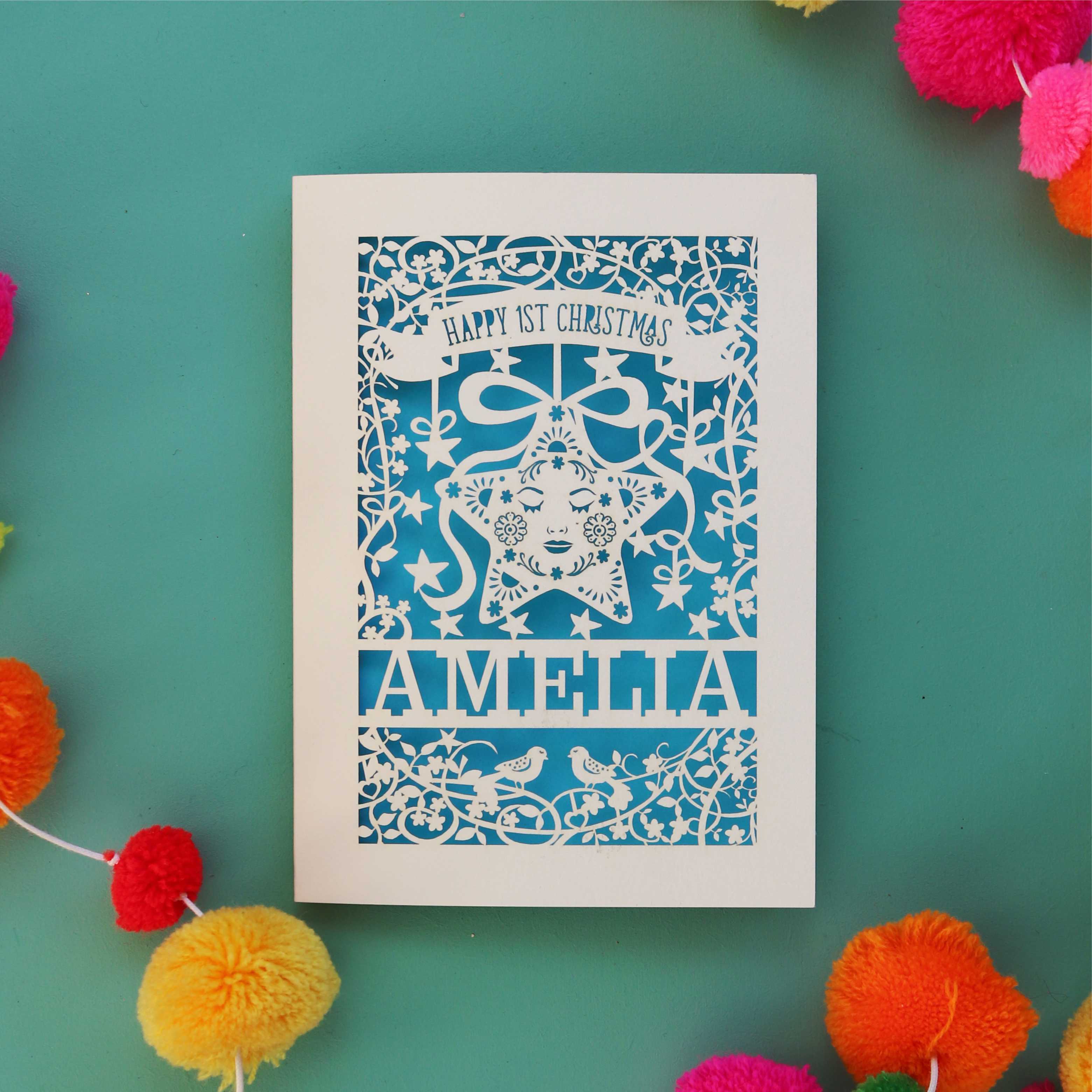 A paper cut 1st Christmas card in cream with a blue paper insert. Card is personalised with a name