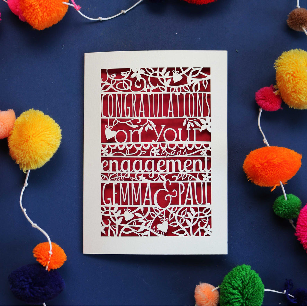 A cream cut out card for engagement, made in the UK. Card says "Congratulations on your engagement" and is personalised with the names of the couple