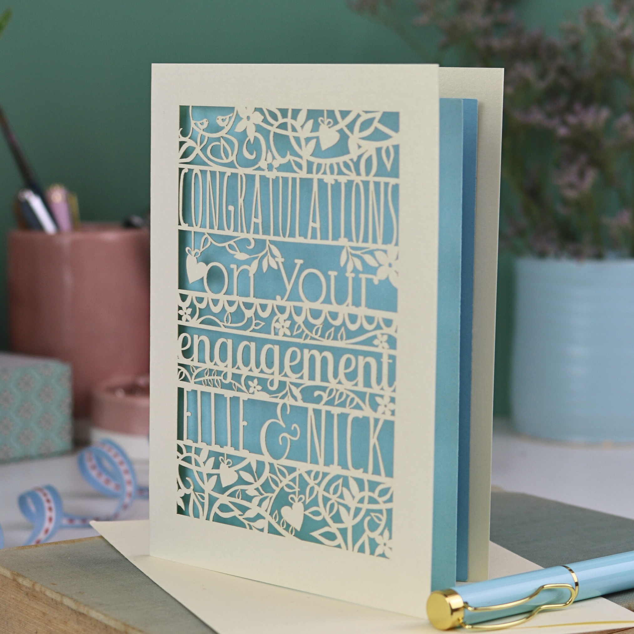 Engagement card with personalized text on a book with stationery items in the background