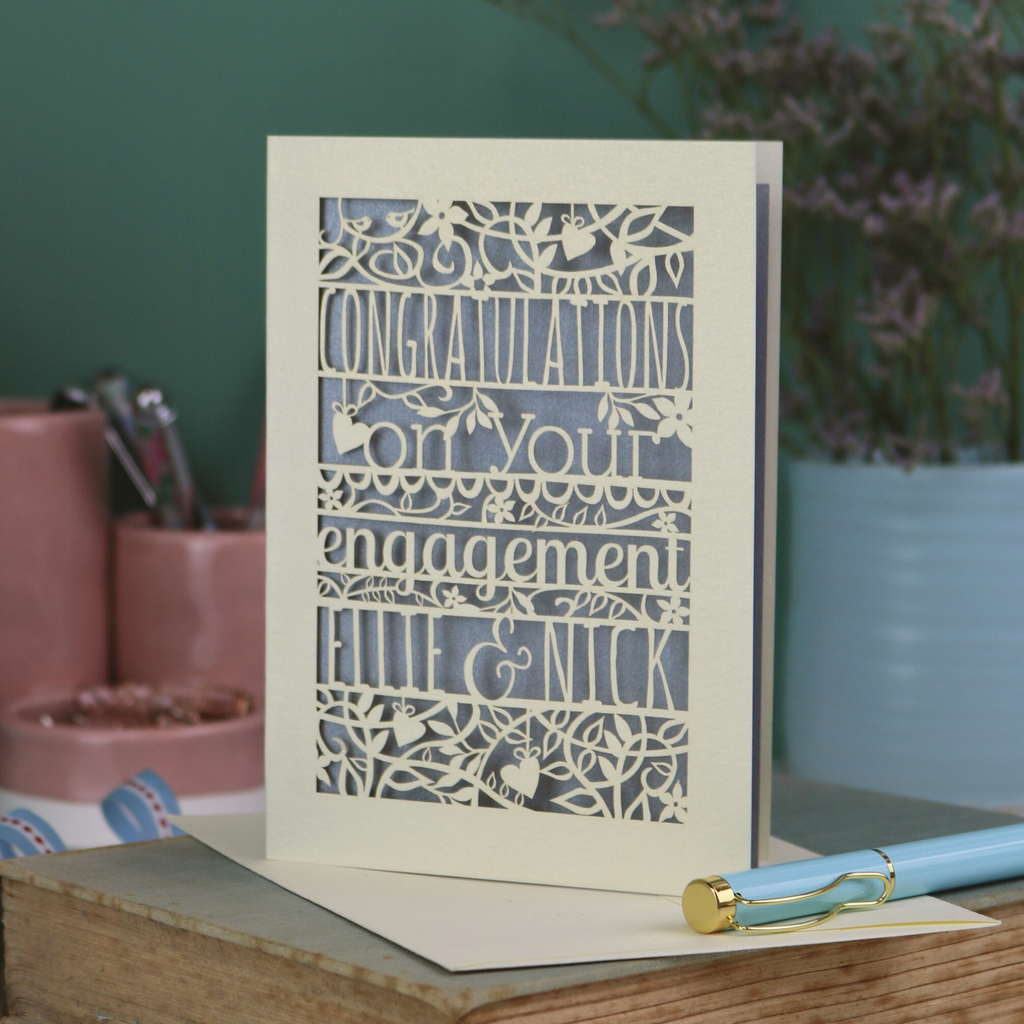 Engagement card with decorative text on a wooden surface with stationery items.
