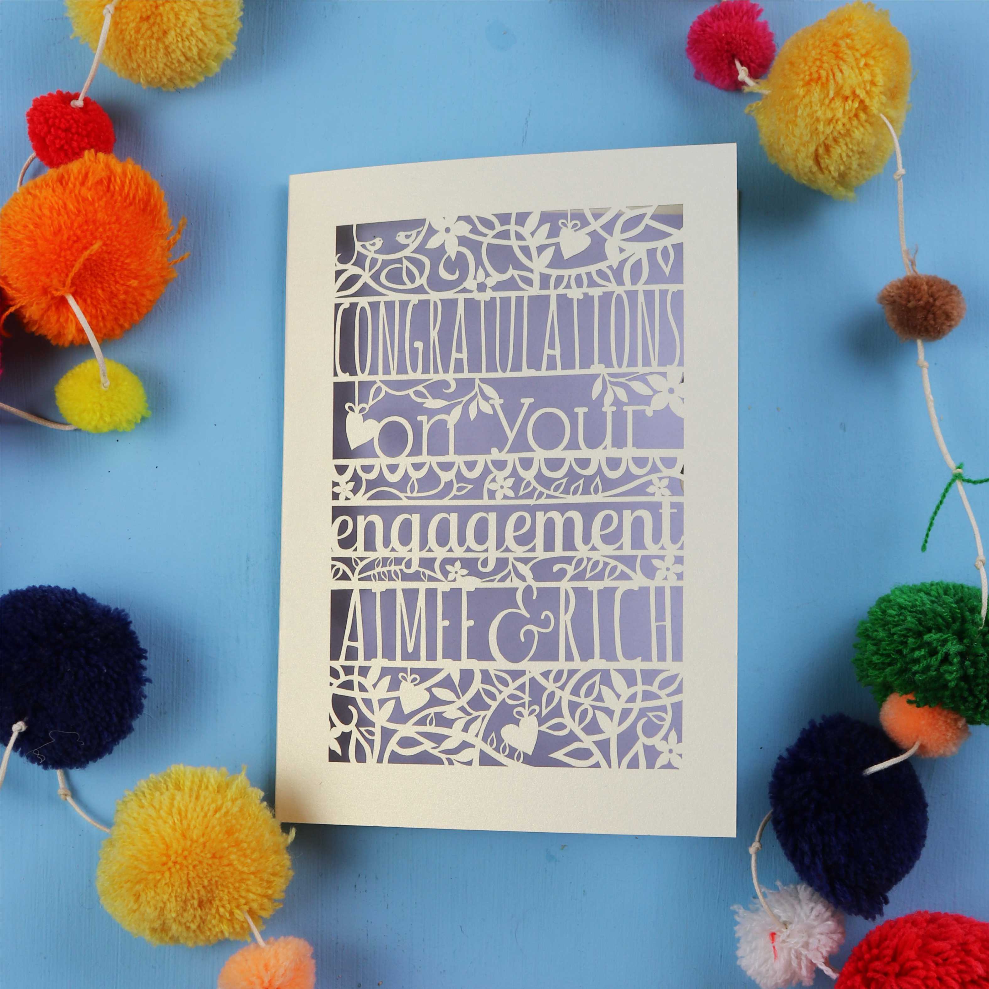 Unique luxury laser cut engagement Card with 'Congratulations on your engagement' text on a blue background with colourful pom-poms.