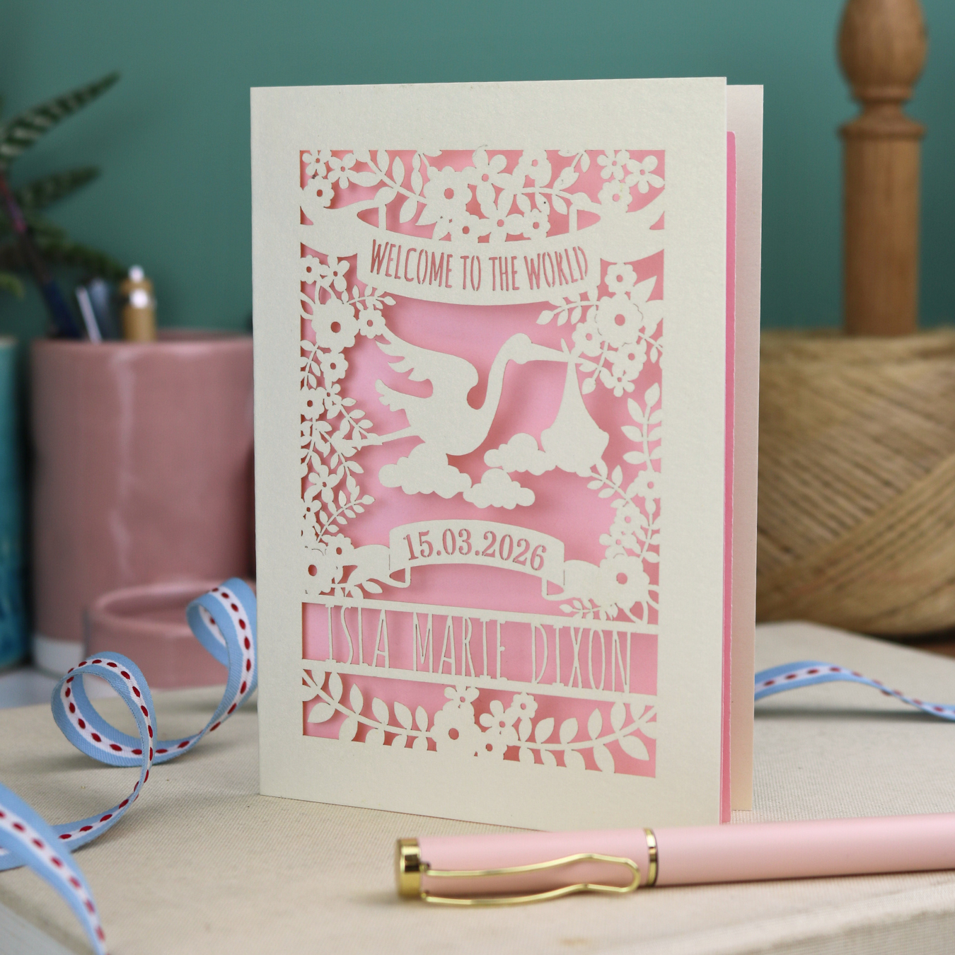 A personalised new baby card with laser cut floral stork design and "Welcome to the World" in cut out text in a banner, with the baby's date of birth and name