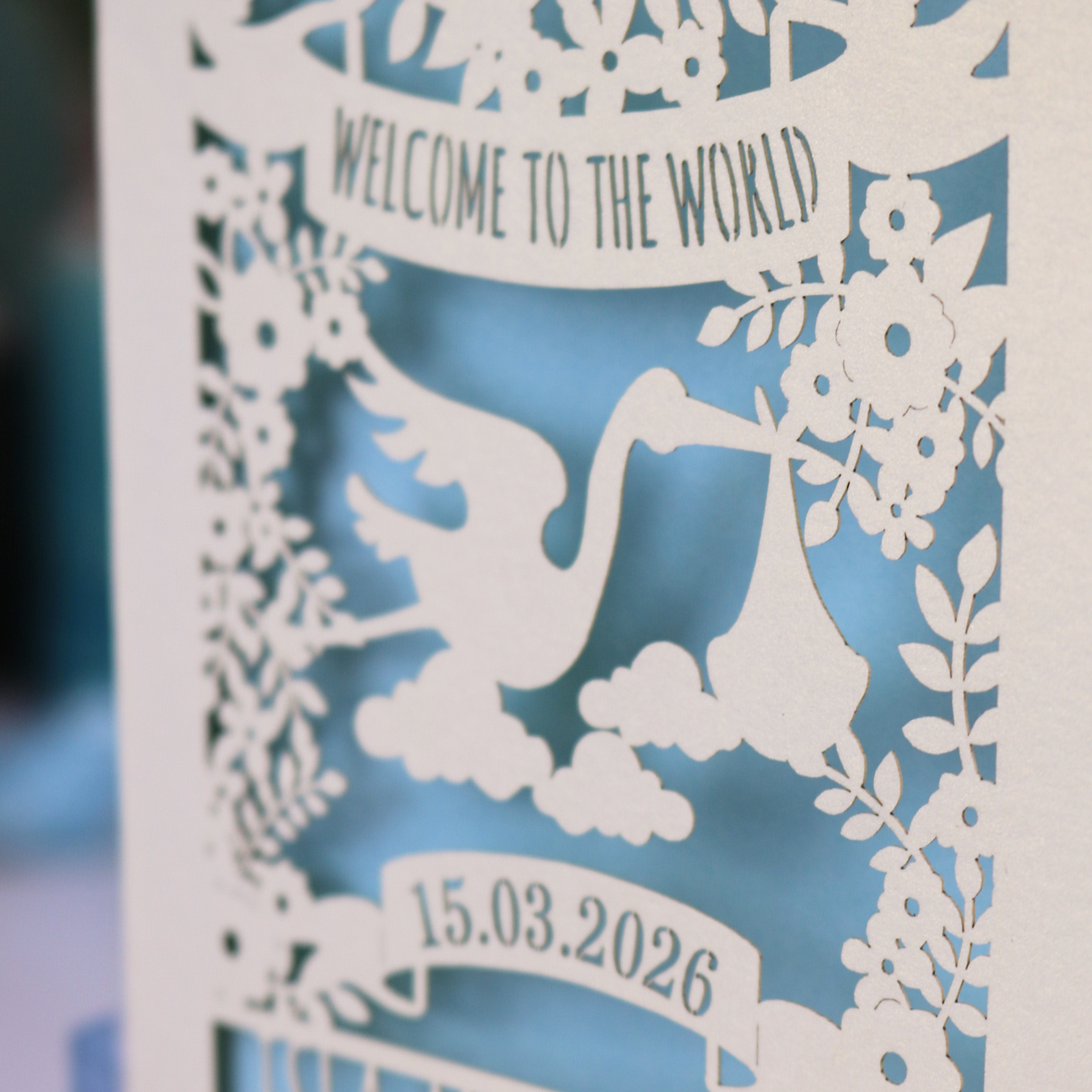 A personalised new baby card with laser cut floral stork design and "Welcome to the World" in cut out text in a banner, with the baby's date of birth and name