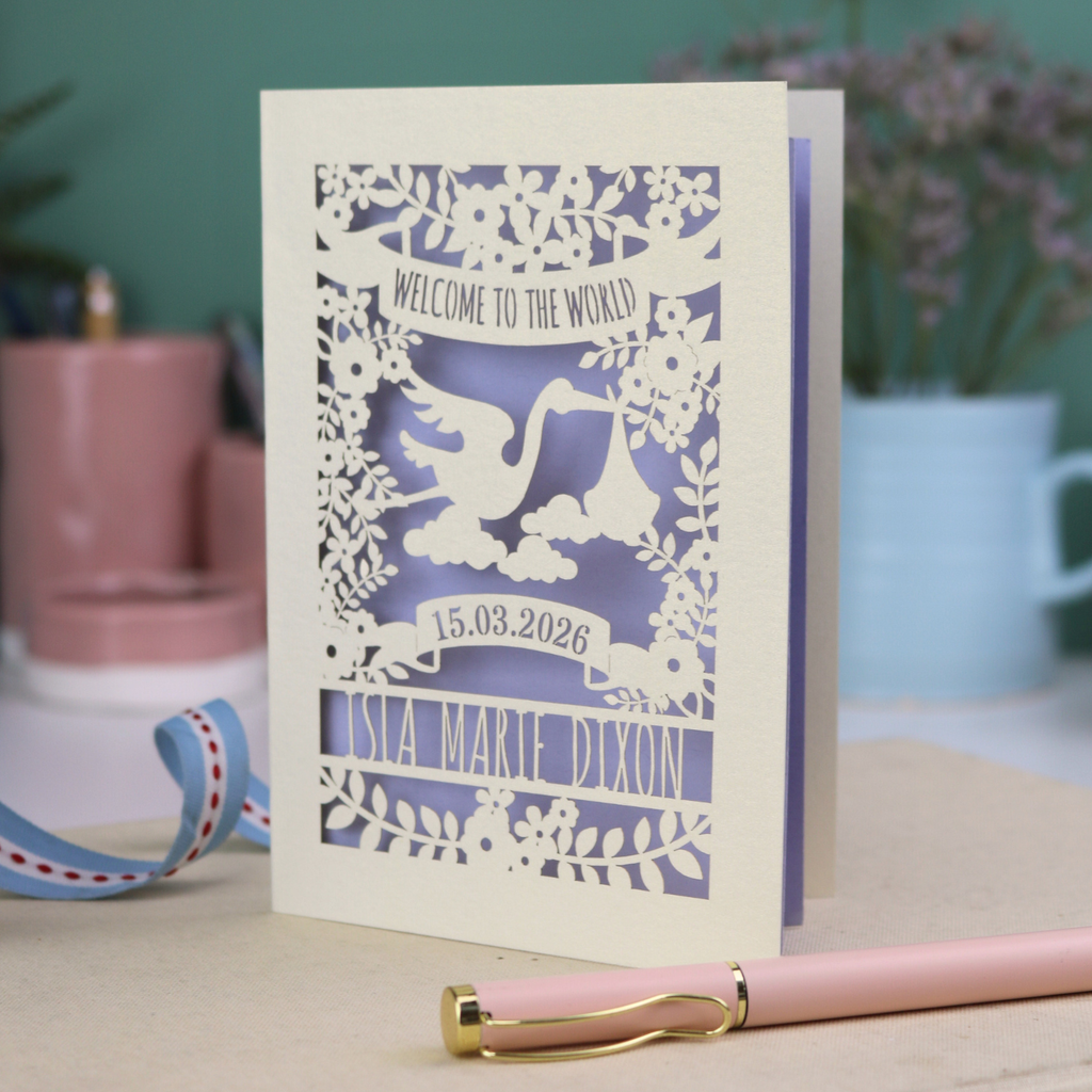 A personalised new baby card with laser cut floral stork design and "Welcome to the World" in cut out text in a banner, with the baby's date of birth and name