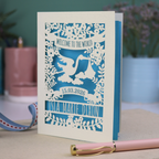 A personalised new baby card with laser cut floral stork design and "Welcome to the World" in cut out text in a banner, with the baby's date of birth and name